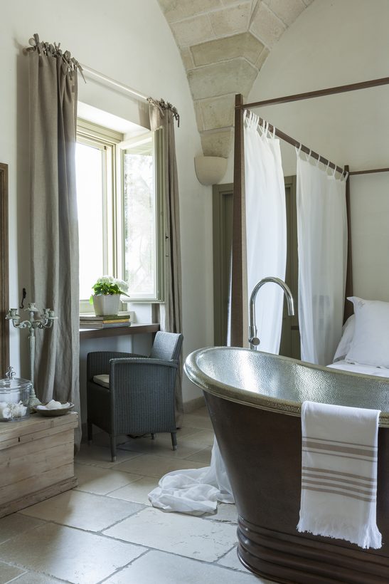 Masseria — copper and tin bath beneath the vaulted stone ceiling, four-poster beyond