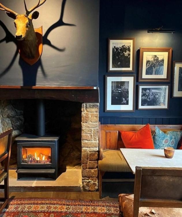 The Nevill Arms — stag and framed bottle-kicking photographs above the lit inglenook, oak settle